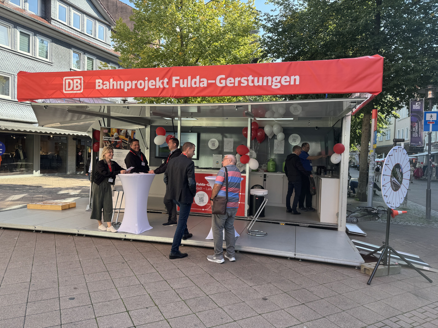 Infomobil mit rotem Banner oben drauf. Text: Bahnprjekt Fulda-Gerstungen. Im Infomobil und davor stehen mehrere Personen