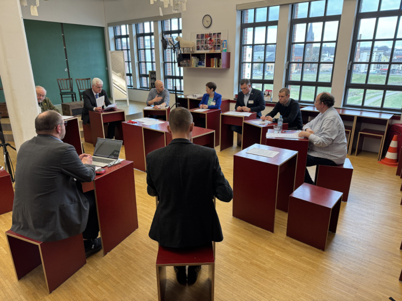 Mitglieder der AG Parlamentarische Befassung sitzen an roten Holztischen und diskutieren.